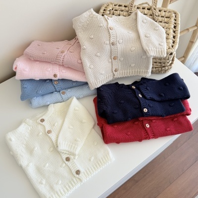 Casacos de malha de bebé em várias cores com botões de madeira colocados sobre uma superfície branca