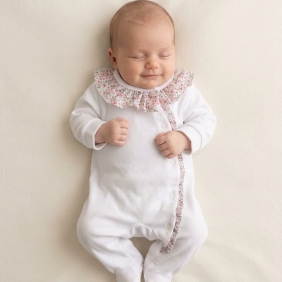 Bebé deitado com macacão branco e detalhes florais na gola e lateral