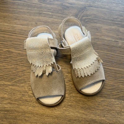 Sandálias infantis castanhas com abas decorativas claras sobre madeira