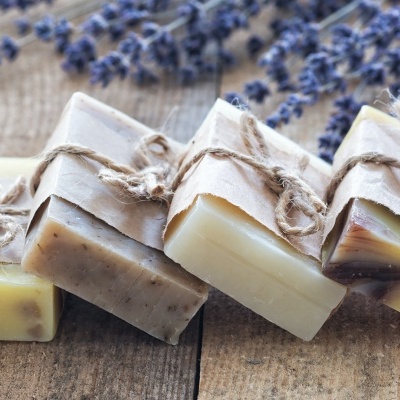 Quatro barras de sabão artesanais amarradas com cordão de juta sobre superfície de madeira, com lavanda ao fundo