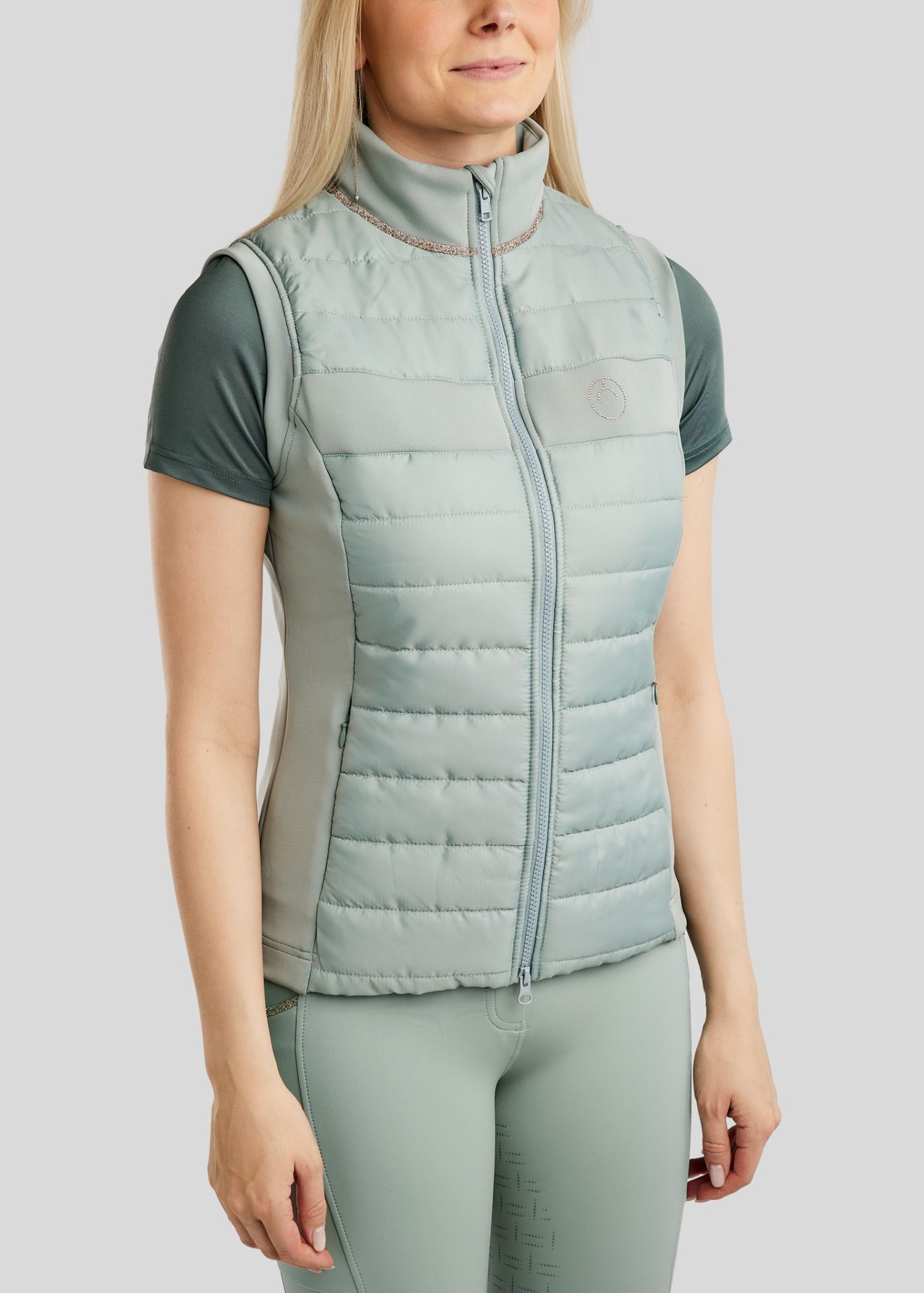 Colete de Senhora MONTAR Lila Colete feminino matelassê verde água com zíper e gola alta, usado com t-shirt manga curta verde musgo e leggings verde água.