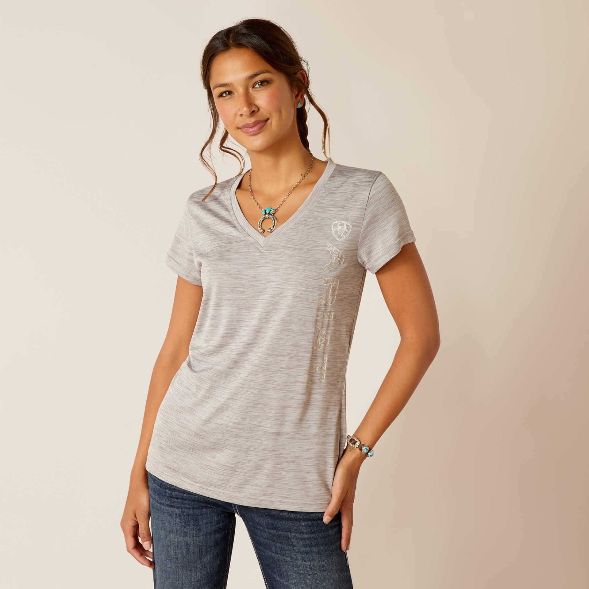 T-Shirt de Senhora ARIAT "Laguna" SS24 Mulher com t-shirt cinza claro de manga curta e decote em V, com jeans e acessórios prateados