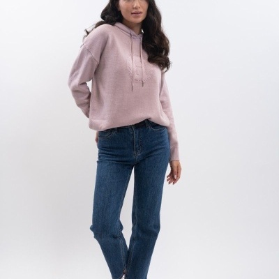 Mulher com camisola de capuz rosa claro, calças de ganga azuis e ténis cor de rosa num fundo branco