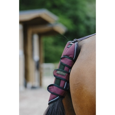 Protector vermelho escuro para rabo de cavalo com detalhes a preto, aplicado no cavalo junto a estrutura de madeira