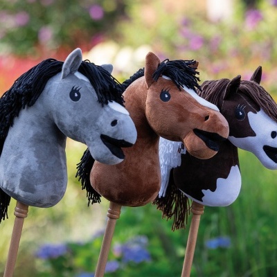 Três brinquedos de cavalo de pelúcia em paus de madeira ao ar livre