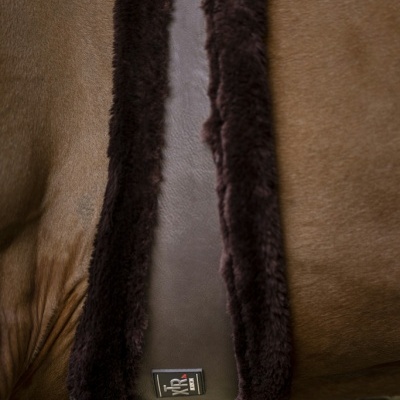 Cinta de sela castanha em pele com bordas de pêlo castanho escuro num cavalo