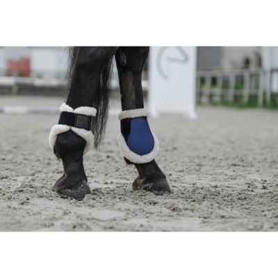 Pernas de cavalo com proteções azuis e brancas em solo arenoso
