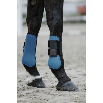Patas de cavalo com protetores azuis e pretos em superfície de areia