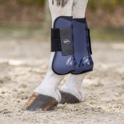Botas azuis QHP para cavalos nas pernas de um cavalo com tiras pretas e solo de areia.