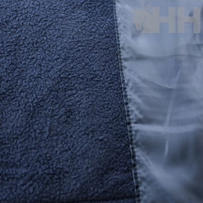 Detalhe de tecido azul escuro com fleece e material liso e costura visível, marca HH em relevo