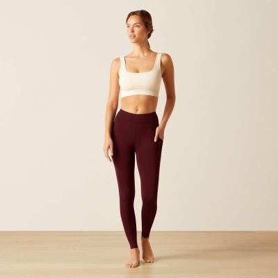 Mulher com top branco e leggings borgonha em fundo neutro