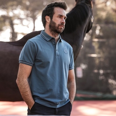 Homem com camisa polo azul claro e cavalo castanho ao fundo num campo de ténis