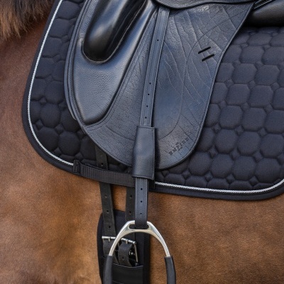 Sela de equitação preta em couro sobre cavalo castanho com alforge acolchoado preto e estribo metálico.