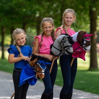 Três meninas com cavalos de pau coloridos ao ar livre.