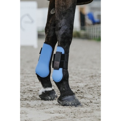 Pernas de cavalo com botas protetoras azuis e pretas no chão de areia