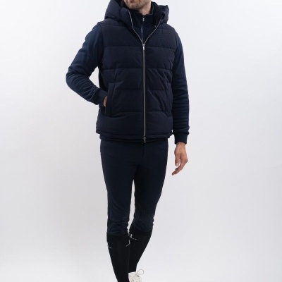 Homem com colete acolchoado azul escuro, calças justas e sapatilhas brancas em fundo branco