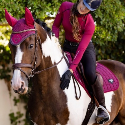 Cavaleira com roupa rosa magenta e capacete azul escuro montada em cavalo castanho e branco com equipamento rosa magenta