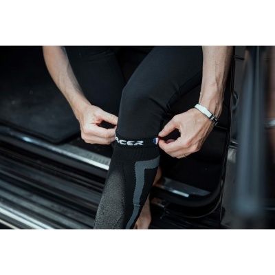 Pessoa vestindo leggings pretas com padrões cinza e texto RACER sentado numa viatura preta.