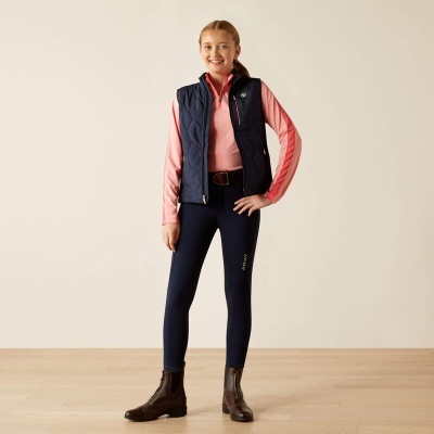 Criança com colete azul, sweat rosa, calças azuis com texto e botins castanhos