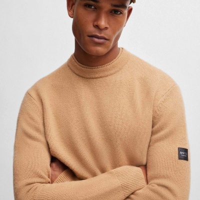 Homem com camisola de malha bege e boné bege com texto BOSS