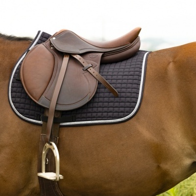 Sela de pele castanha sobre manta preta num cavalo castanho.