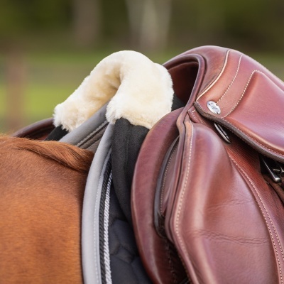 Sela de equitação castanha com forro felpudo creme numa sela sobre cavalo