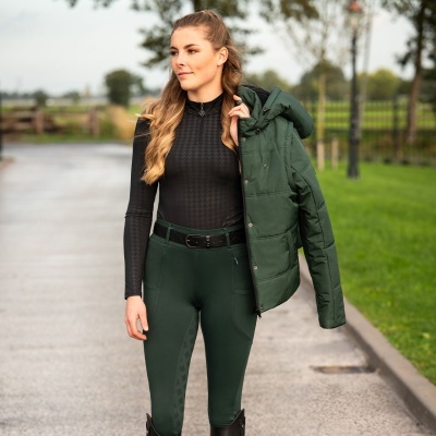 Mulher com camisa preta, calças verdes e casaco verde acolchoado ao ar livre