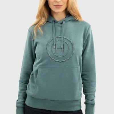 Mulher com sweatshirt verde-água com capuz e bolso frontal, logótipo em relevo, calças jeans escuras, fundo cinzento claro