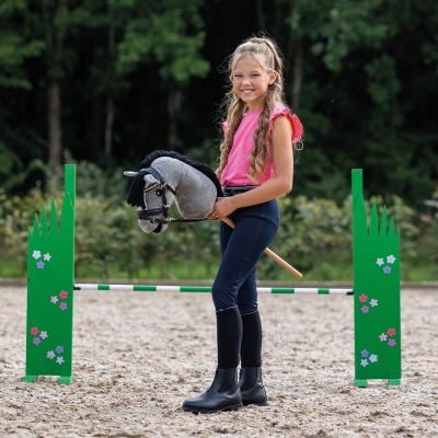 Menina com cavalo de brinquedo em pista de equitação com obstáculos verdes