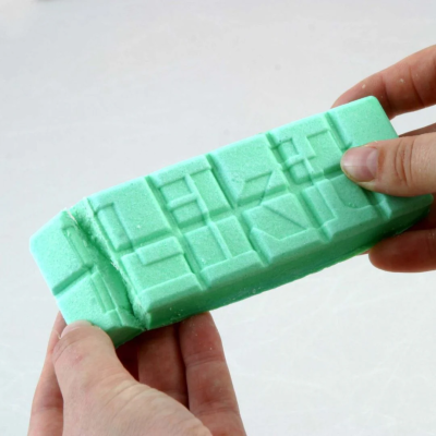 Bloco azul claro com padrões geométricos segurado por duas mãos