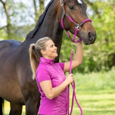 Mulher com colete rosa a segurar rédea cor-de-rosa em cavalo castanho na natureza
