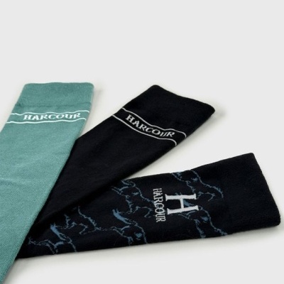 Três pares de meias em cores verde, preto liso e preto com padrão azul com texto HARCOUR.