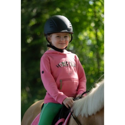 Criança com capacete preto e hoodie rosa a cavalo com sela rosa em ambiente natural