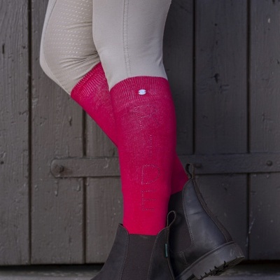 Meias de equitação rosas com calças bege e botas de couro preto junto a um portão de madeira escura