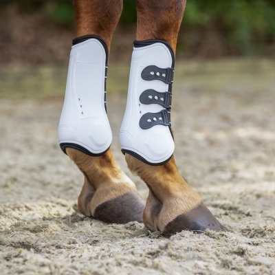 Proteções para pernas de cavalo brancas com fivelas pretas nas patas de um cavalo no chão de areia