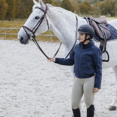 Mulher com roupa de equitação segurando rédea de cavalo branco com sela