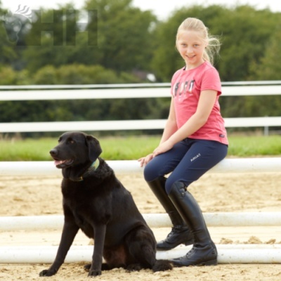 Menina com roupa de equitação e cão preto sentado ao ar livre junto a vedação branca