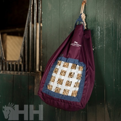 Saco de alimentação para cavalos roxo com grelha branco-azul pendurado em porta verde de estábulo