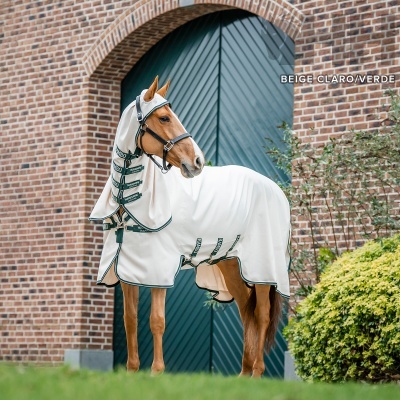 Cavalo vestido com manta branca com detalhes verdes e bege claro em frente a porta verde e parede de tijolos