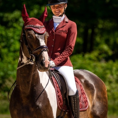 Cavaleira com roupa de equitação a montar cavalo com manta vermelha em cenário natural
