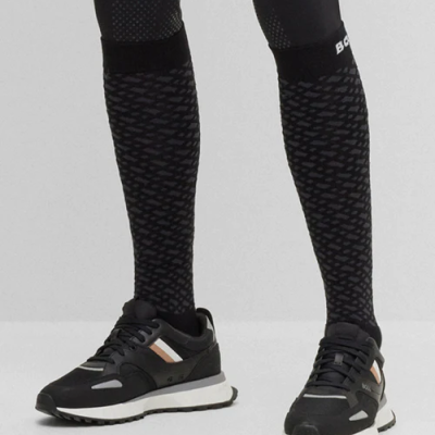 Pernas com meias pretas com padrão cinza e sapatilhas desportivas pretas com detalhes bege e cinza