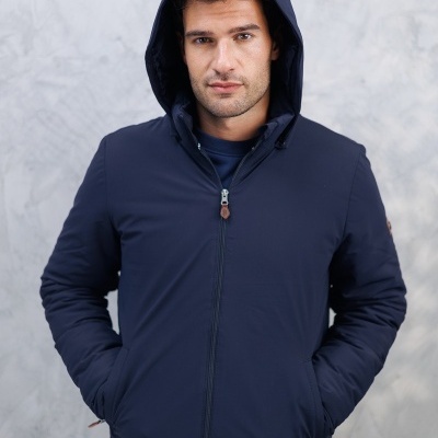 Homem com casaco azul escuro com capuz e fecho de correr em fundo cinzento