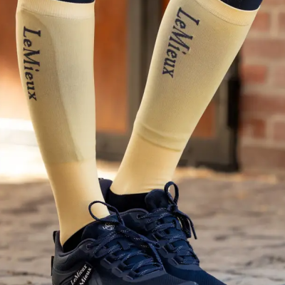 Pernas com meias amarelas LeMieux e sapatilhas pretas LeMieux em piso de pedra