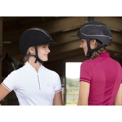 Duas mulheres com capacetes pretos e camisetas de equitação branca e rosa num estábulo