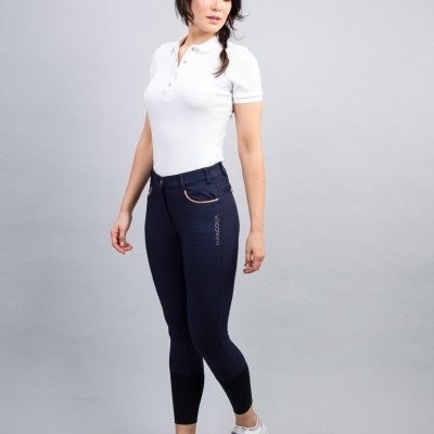 Mulher com polo branca e leggings azul escuro de montaria em fundo cinza