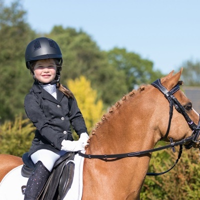 Menina com roupa de equitação montada num cavalo castanho ao ar livre