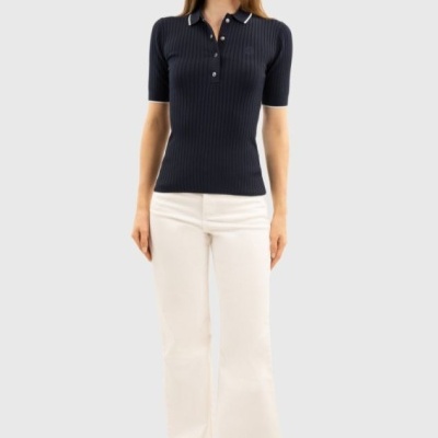 Mulher de pé com polo preta canelada e calças brancas