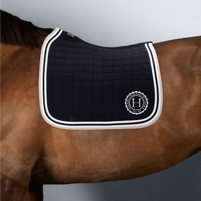 Manta azul escura acolchoada para cavalo com bordas claras e emblema branco com H sobre cavalo castanho