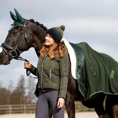 Mulher de casaco verde ao lado de cavalo com manta verde