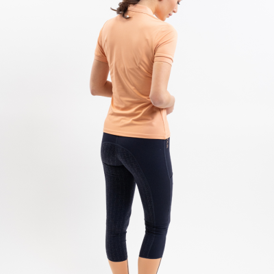 Mulher de costas vestindo polo cor de pêssego e calças desportivas azul escuro com detalhes cor de pêssego